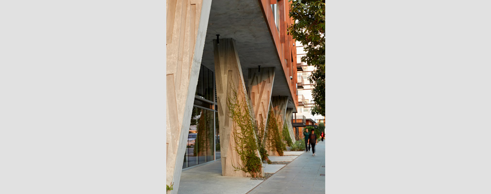 Photograph of the first floor of a building, with angled concrete columns along the sidewalk supporting the building’s upper stories.