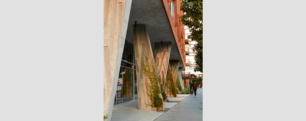 Photograph of the first floor of a building, with angled concrete columns along the sidewalk supporting the building’s upper stories.