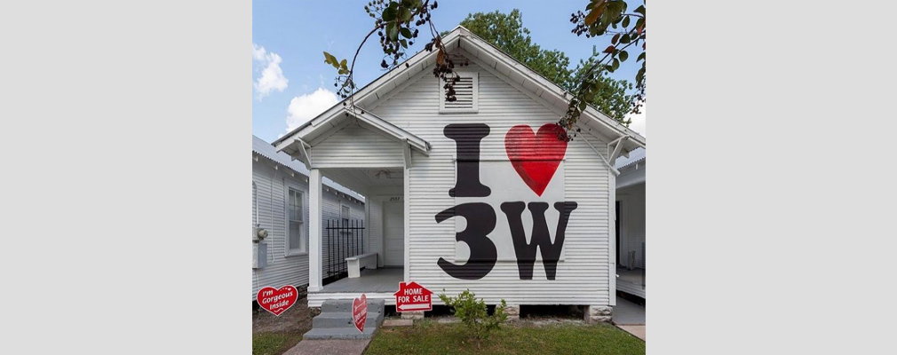 Photograph of the front façade of a shotgun house painted with the phrase “I ❤ 3W,” with temporary signs in the front lawn saying, “I’m Gorgeous Inside,” “Open House,” and “HOME FOR SALE.”