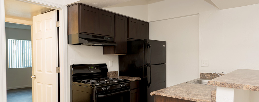 Photograph of a kitchen with a sink in a peninsula opposite a stove and refrigerator along a wall with upper and lower cabinets.