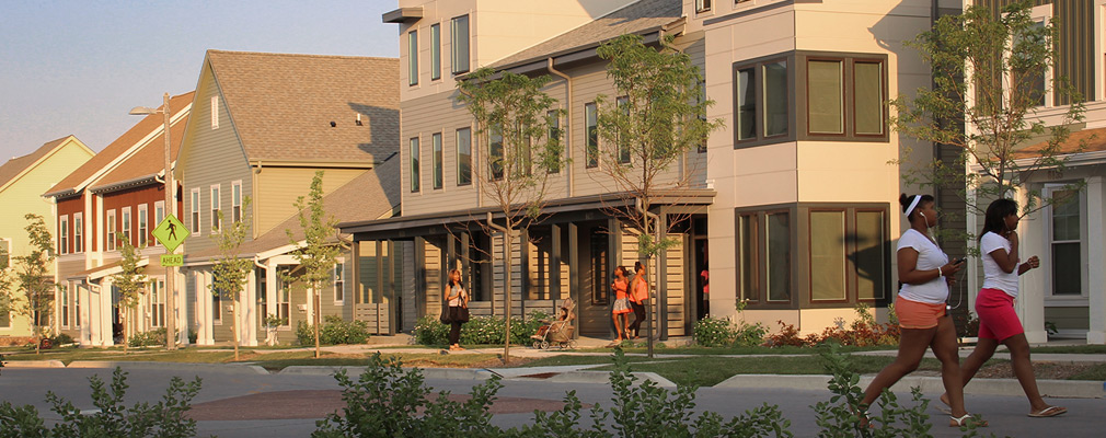 Photograph of the front façades of several two- and three-story residential buildings along a local street.