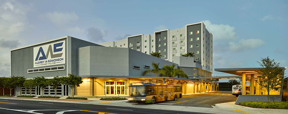 Photograph of a two-story building, with two buses in the loading area beside the building.