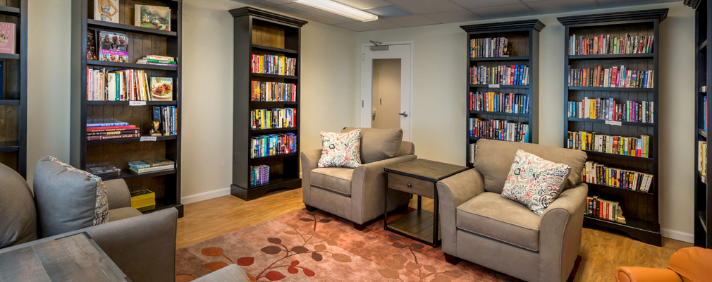 Photograph of a library lined with shelves of books and furnished with armchairs. 