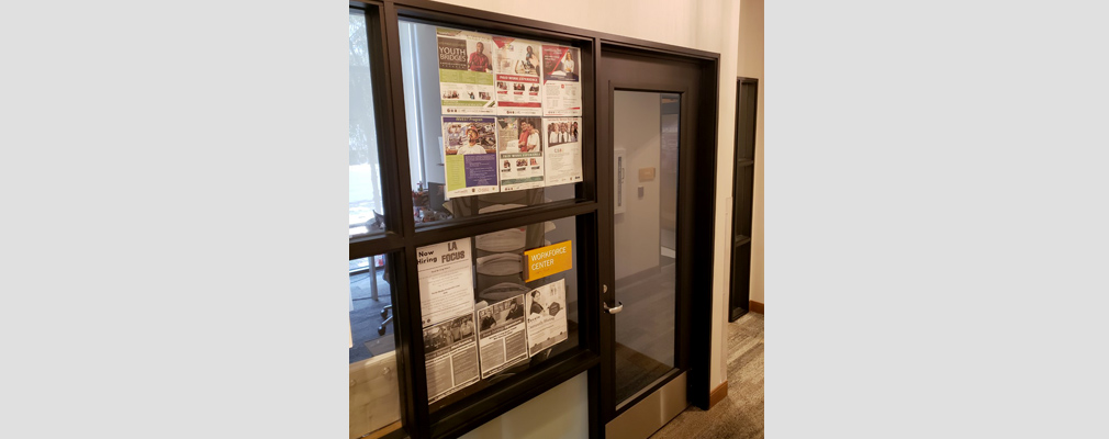 Photograph of the door of the workforce center, with job postings taped to the office window.