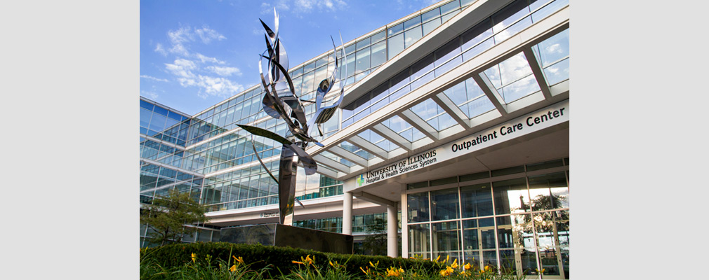 Photograph of a multistory medical building, with a sign reading “University of Illinois Hospital & Health Sciences System Outpatient Care Center” above the entrance and with a metal sculpture in the foreground.