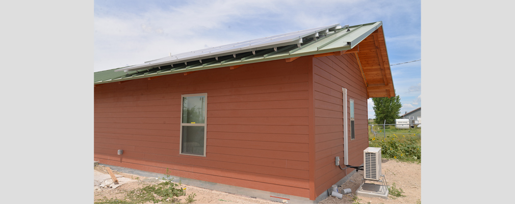 Photograph of the back and side façades of a one-story house with rooftop solar panels.