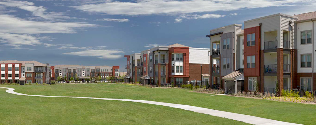 Photograph of several apartment buildings, with a connecting path meandering through a grassy area.