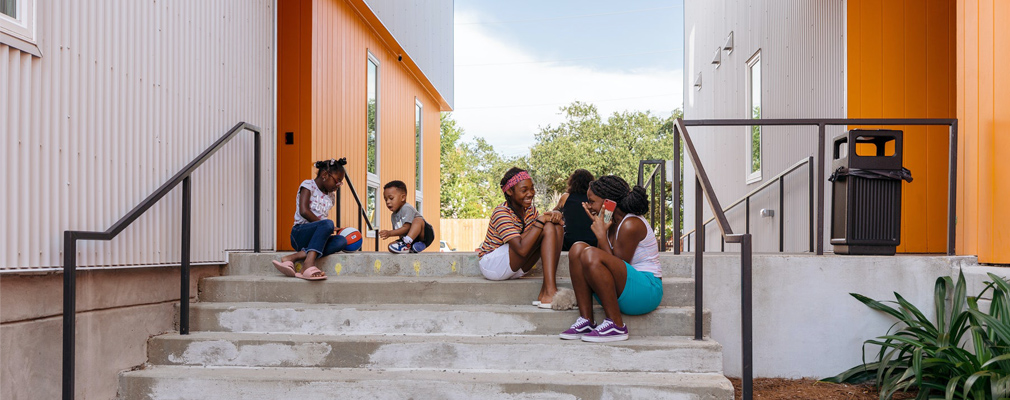 Photograph of five children sitting outdoors on steps between two wings of a three-story apartment building.