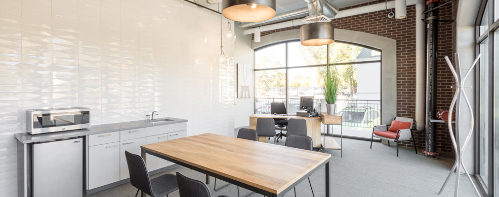 Photograph of the 9th East Lofts leasing office, a room with a kitchenette and table, a desk, and floor-to-ceiling windows along two walls.