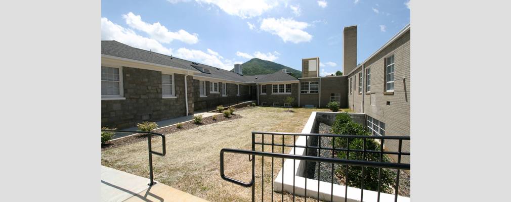 Photograph of a landscaped courtyard framed by the two sections of the historic building, with a paved walkway and railings in the foreground.  