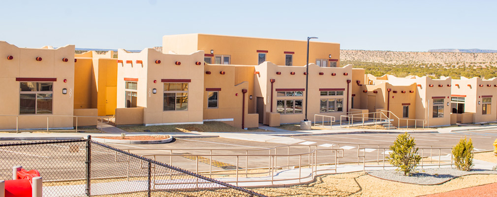 Photograph of several attached residences, with courtyards at the units’ entrances. Doors on the upper floor of the two 2-story units provide access to patios on first-floor roofs.