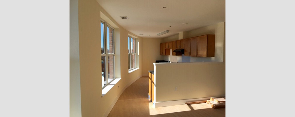 Photograph of a kitchen taken from the living area, with two large windows in a side wall.