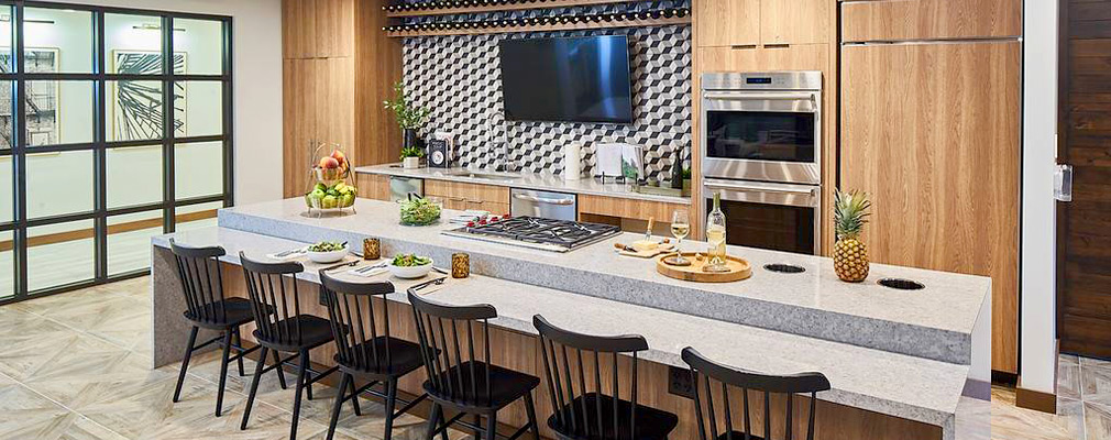 Photograph of a kitchen with a two-tier island lined with six chairs on one side.