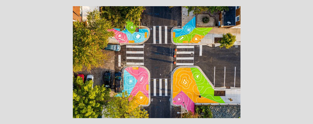 Aerial photograph of an intersection with new landscaping, crosswalks, and traffic-calming measures, including brightly painted curb extensions.