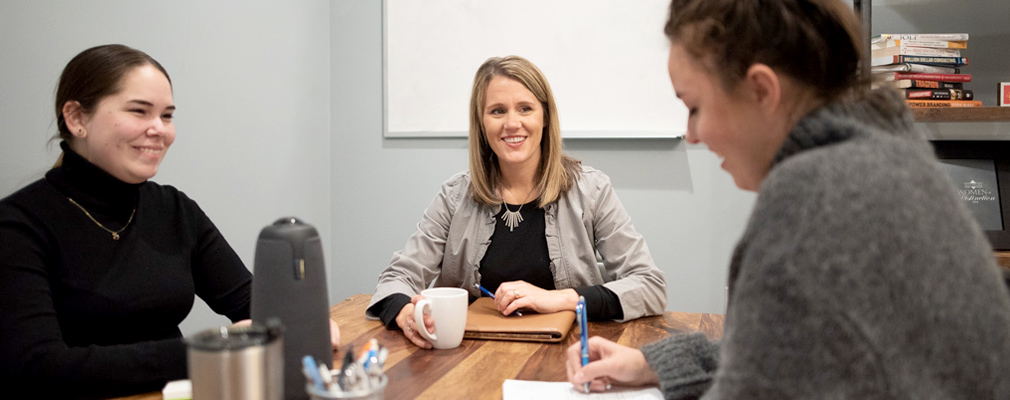 Photograph of three women seated at a conference table.