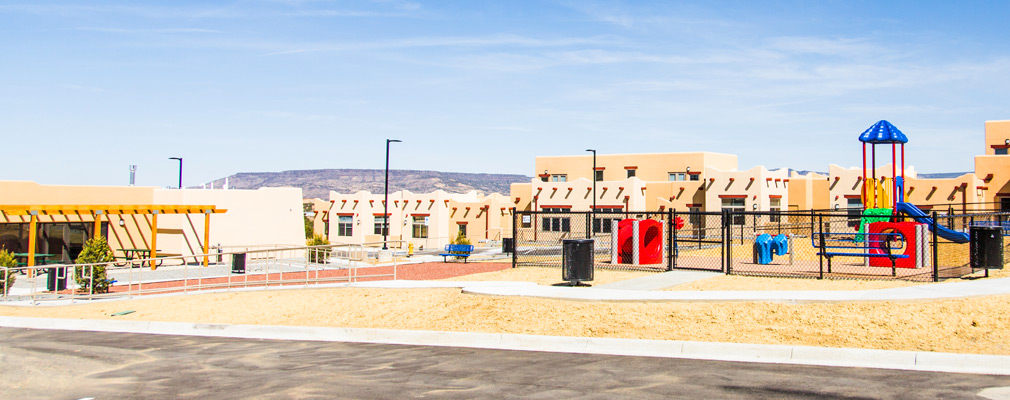 Photograph of the single-story community building (left) and playground (right), with attached residences in the background.