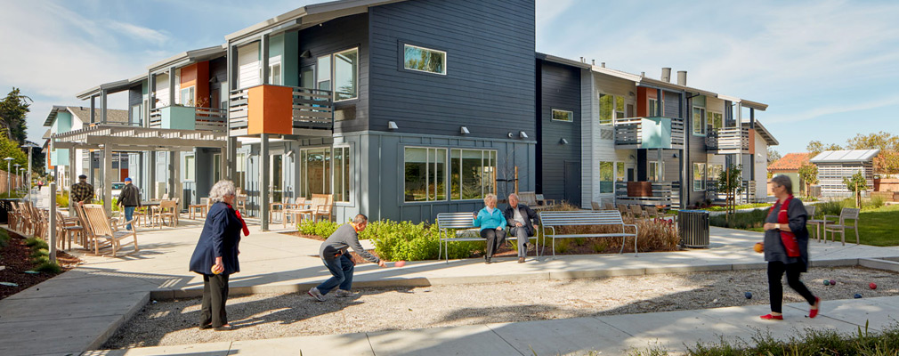 Photograph of several residents watching and playing bocce ball beside a two-story residential building.