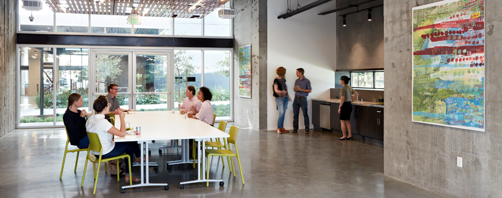 Photograph of a common area with artwork hanging on a wall near a table where five people are seated.