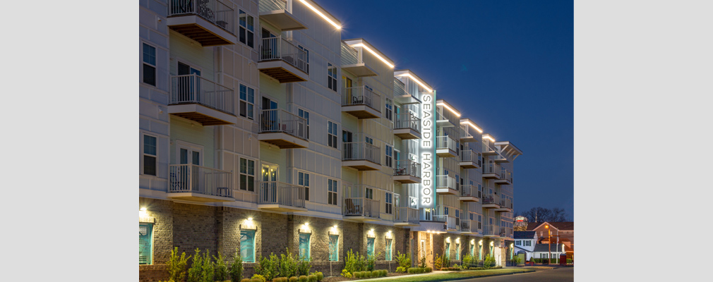 Photograph of the front façade of a multistory apartment building lit up at night, with a projecting sign reading “Seaside Harbor” above the entrance.