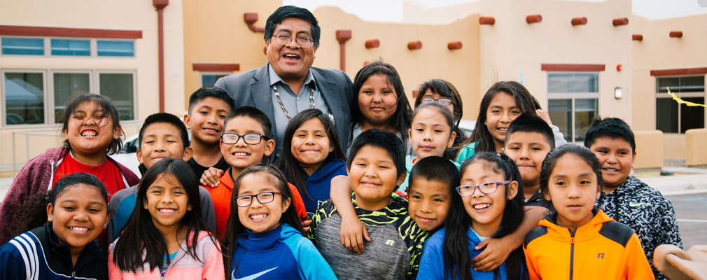 Photograph of 18 children and 1 adult, with attached residences in the background.