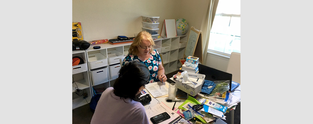 Photograph of two women seated at a table in an office conferring over documents.