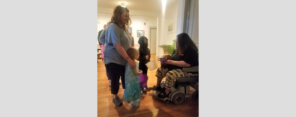 Photograph of a woman seated in a wheel chair giving candy to two costumed children who are accompanied by a woman.  