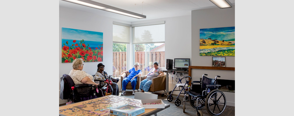 Photograph of four women seated in front of large windows in a corner in a community room.