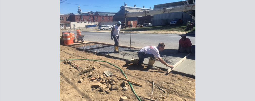 Photograph of three men installing a sidewalk. 