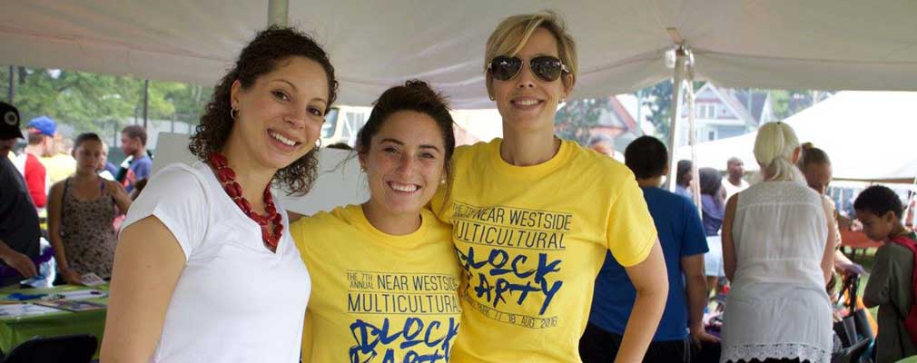 Photograph of three women standing beside information tables underneath a tent.