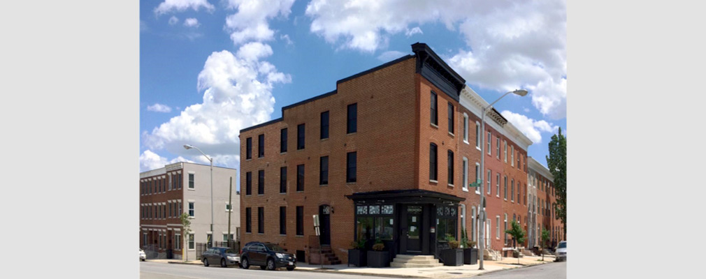 Photograph of the two street façades of a building with a corner storefront on the end of a row of three-story rowhouses. 