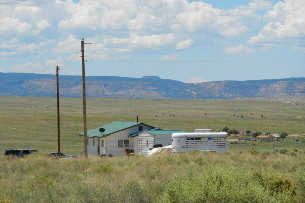 Photo features the side of a single-story house in a rural setting with mountains in the background.