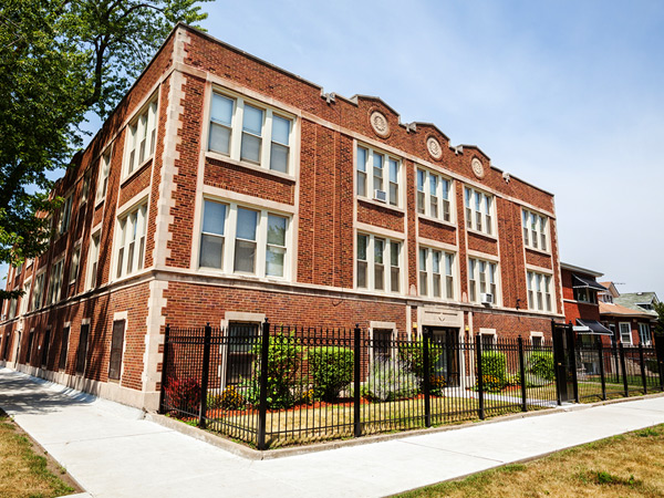 Photo featuring two sides of a three-story brick building with shrubbery along the front.