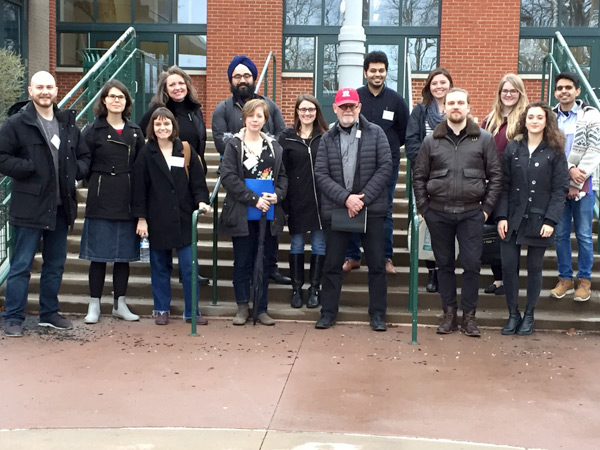 Image of fourteen people standing on the steps in front of a brick building.