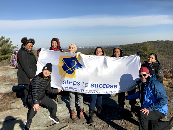 Photograph of seven students and an adult holding a Steps to Success program banner on a hike in the mountains.