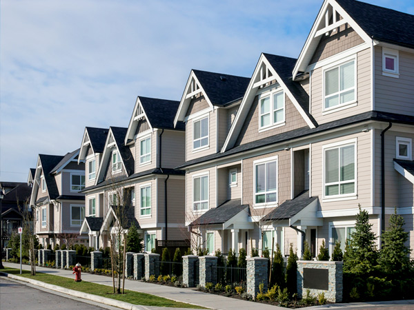 Photograph of three-story townhouses with siding facades along a street.