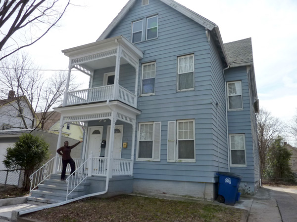 Photograph of a woman standing on the steps of a three-story, multifamily building.