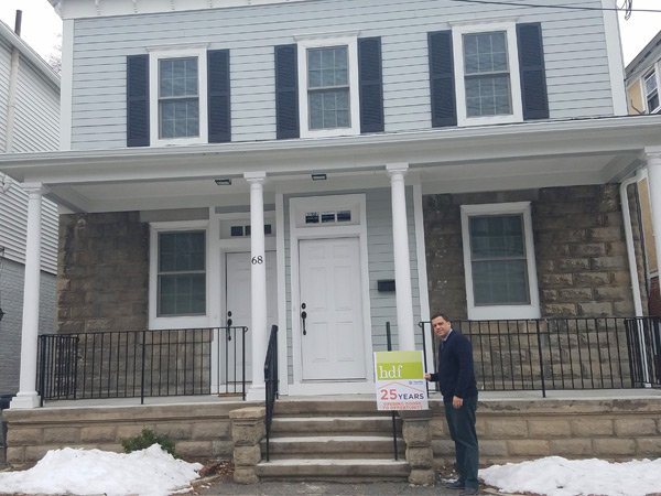 Photograph of a man standing in front of a small multifamily building.