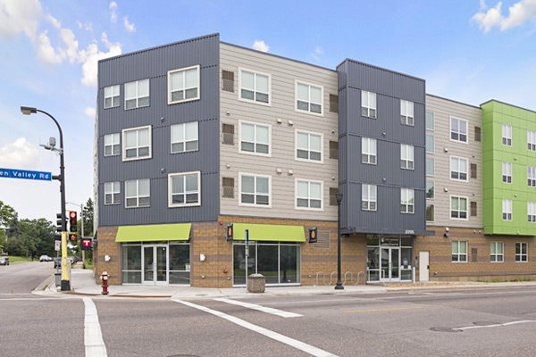 Photograph of a portion of the front façade of a three-story building, including the entrances to the residential portion of the building and to the retail space at the corner of the building.