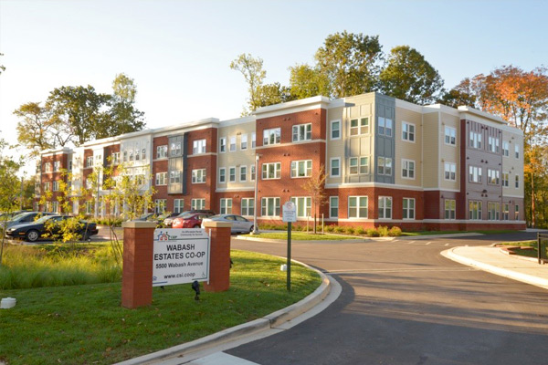 Photograph of the front and side façades of a three-story residential building with a sign in the foreground reading, “Wabash Estates Co-op.”