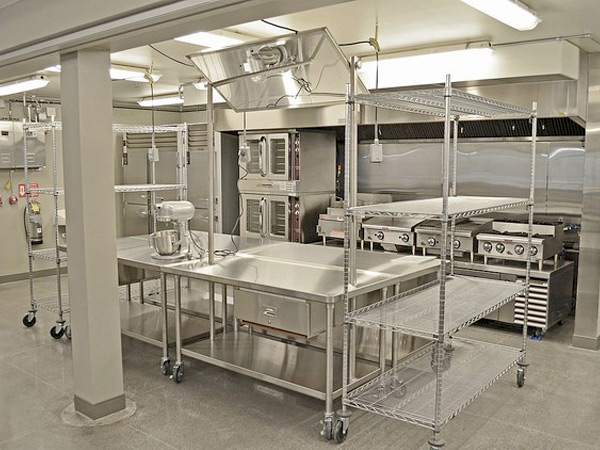 Photograph of a commercial kitchen with stainless steel appliances, tables, and shelving.