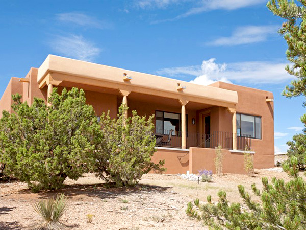 Photograph of a flat-roofed stucco house with a covered porch, framed by evergreen shrubs.