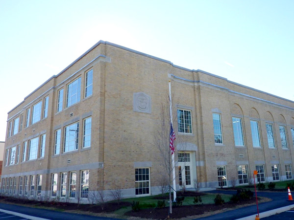 Photograph of the front and side façades of a three-story, yellow brick building with large windows.