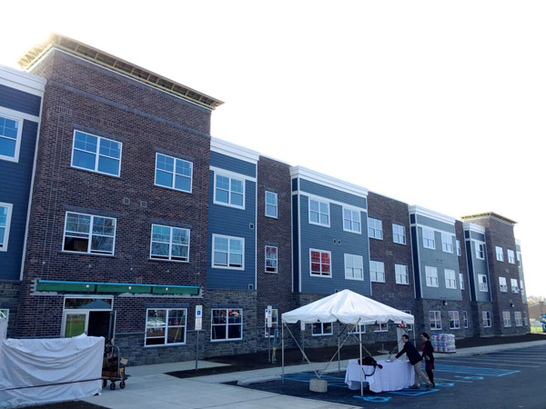 Photograph of the front façade of a flat-roofed, three-story apartment building clad in brick, stone, and siding.