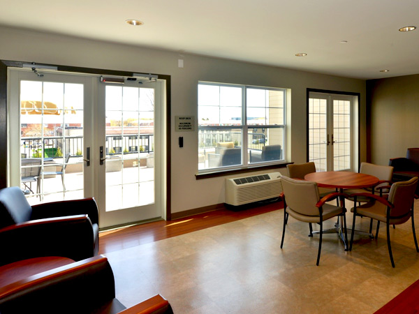 Photograph of a sitting area with chairs and tables separated from a patio by windows and two sets of double French doors.