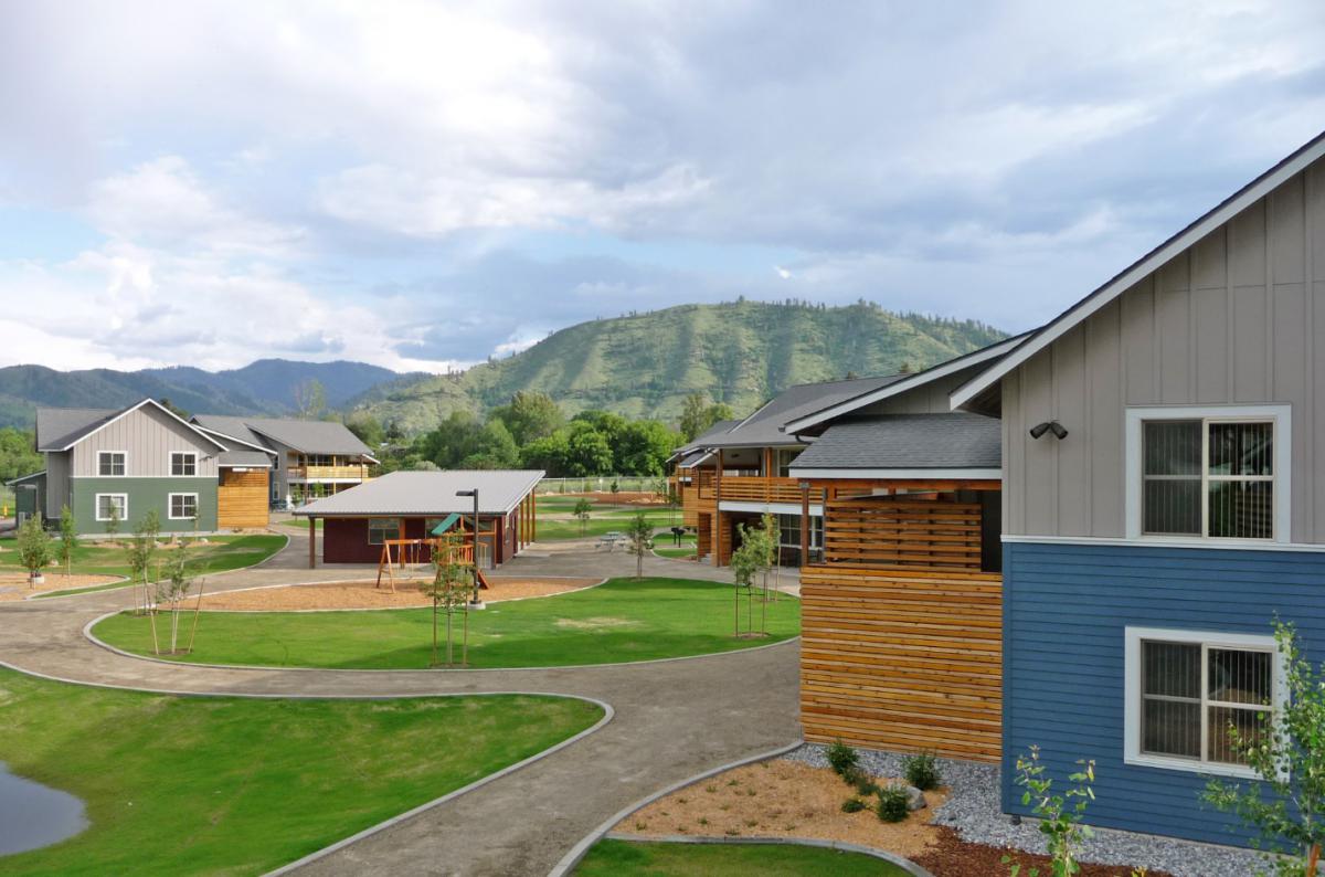 Photograph of several two-story residential buildings surrounding a large open space with a playground and shelter.