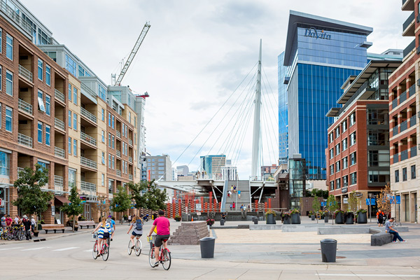 Three people bicycle between two rows of multifamily buildings.