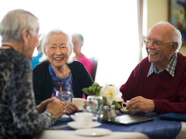 Two older women and a man sit around a small table drinking coffee.