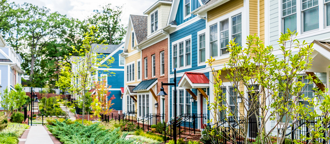 Photograph of a row of town homes with varied facades facing a walk way surrounded by greenery.