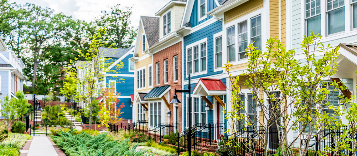 Photograph of a row of town homes with varied facades facing a walk way surrounded by greenery. Photograph of a row of town homes with varied facades facing a walk way surrounded by greenery.