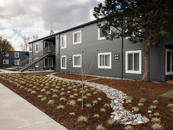 Photograph of two two-story buildings with external staircases and large flowerbeds.